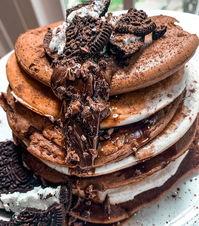 A stack of pancakes topped with chocolate sauce and crushed oreos