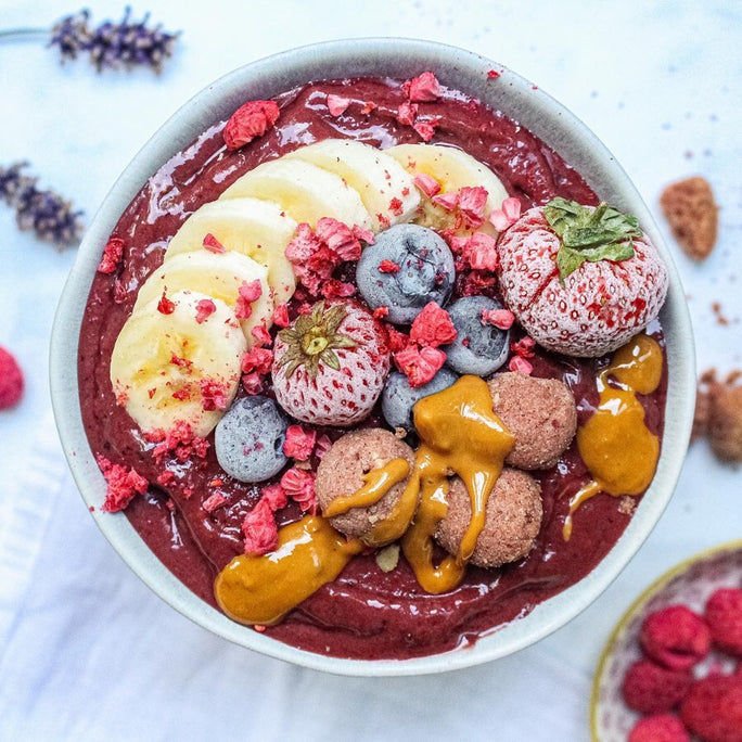 White bowl filled with purple smoothie, protein balls, frozen fruit and bananas