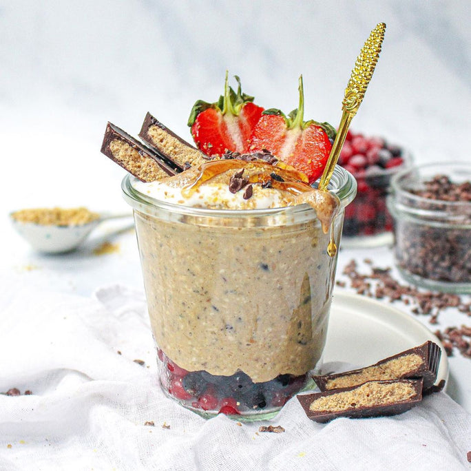 A glass filled with a protein smoothie and topped with fruits, chooclate and syrup