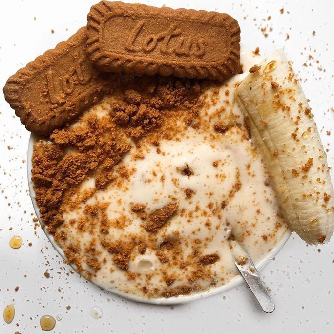 A white bowl filled with vanilla pudding, lotus biscoff biscuits and a banana