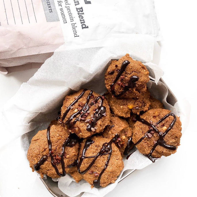 Brown cookies drizzled in chocolate next to a bag of Free Soul protein powder