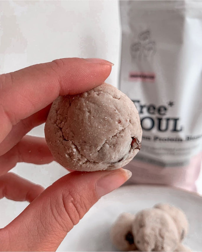 someone holding a proteClose up for a hand holding a protein ball that is a light colourn energy ball above a plate of protein energy balls