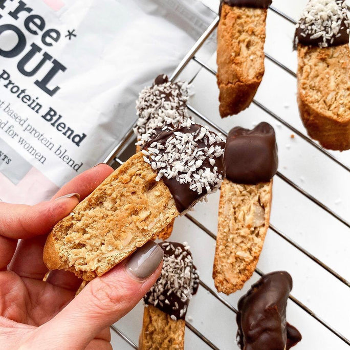 Close up of a hand holding almond biscuits dipped in chocolate and shaved coconut