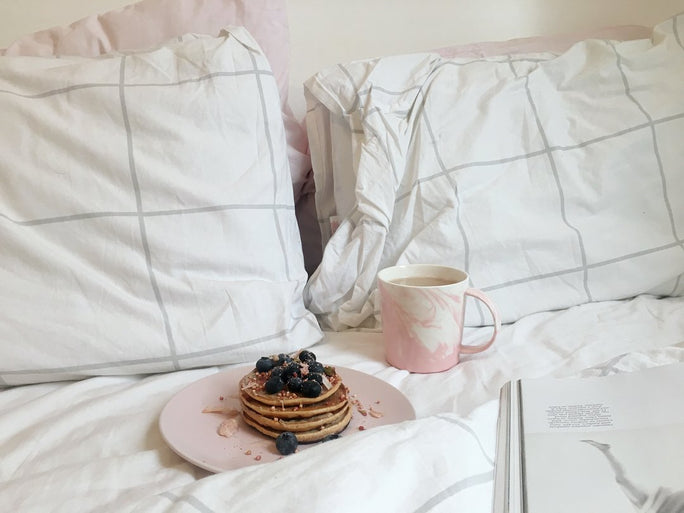 A stack of blueberry pancakes on a white duvet and pillowcase set