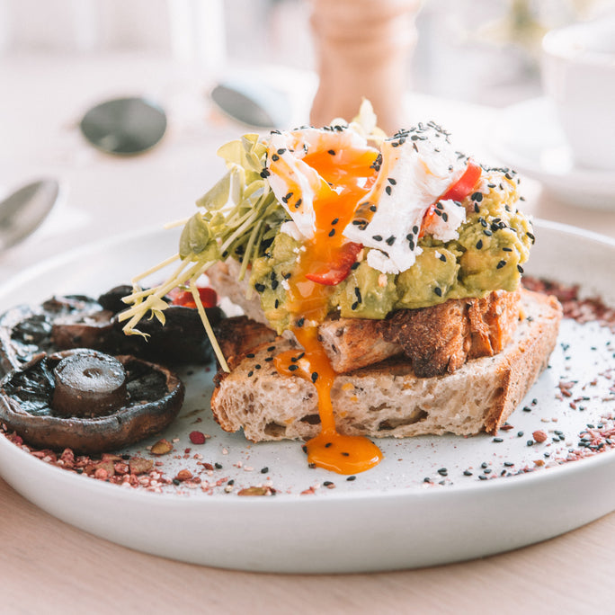 A white plate topped with toasted bread, large mushrooms, avocado and a poached egg