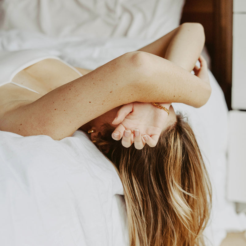 A woman laying in bed with her hair dropping of the edge and hands covering her face