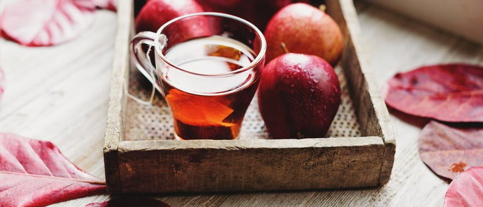 Autumnal leaves scattered around deep red apples and a mug of tea