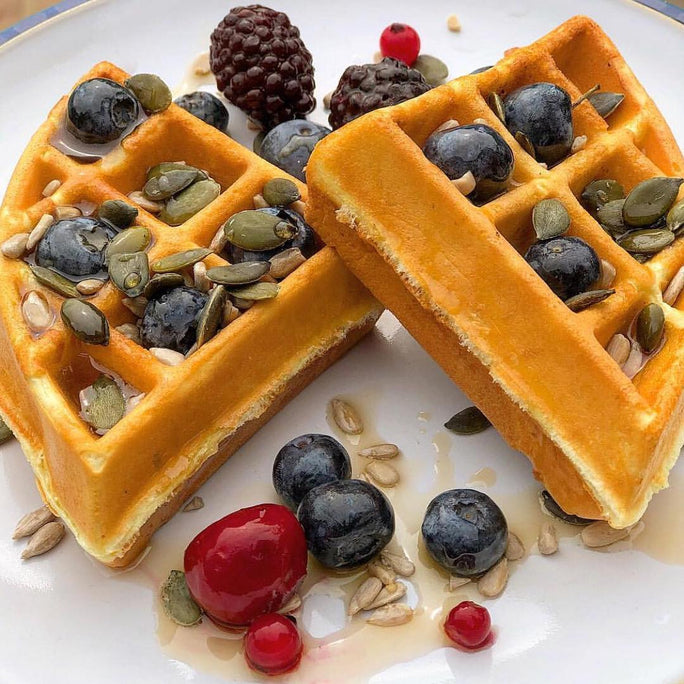 Golden waffles topped with maple syrup, pumpkin seeds and berries