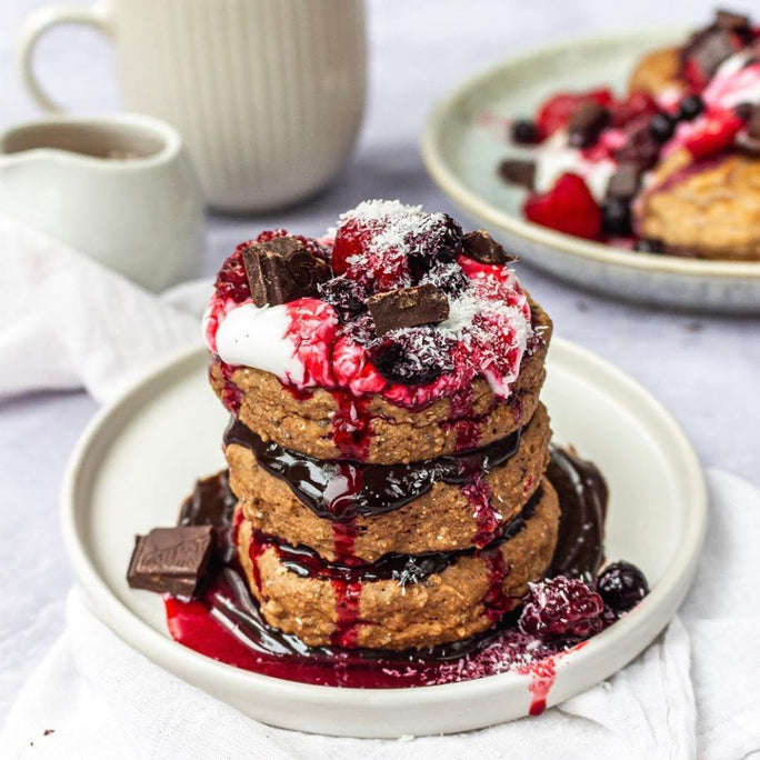 A stack of chocolate pancakes with purple berries and chocolate pieces