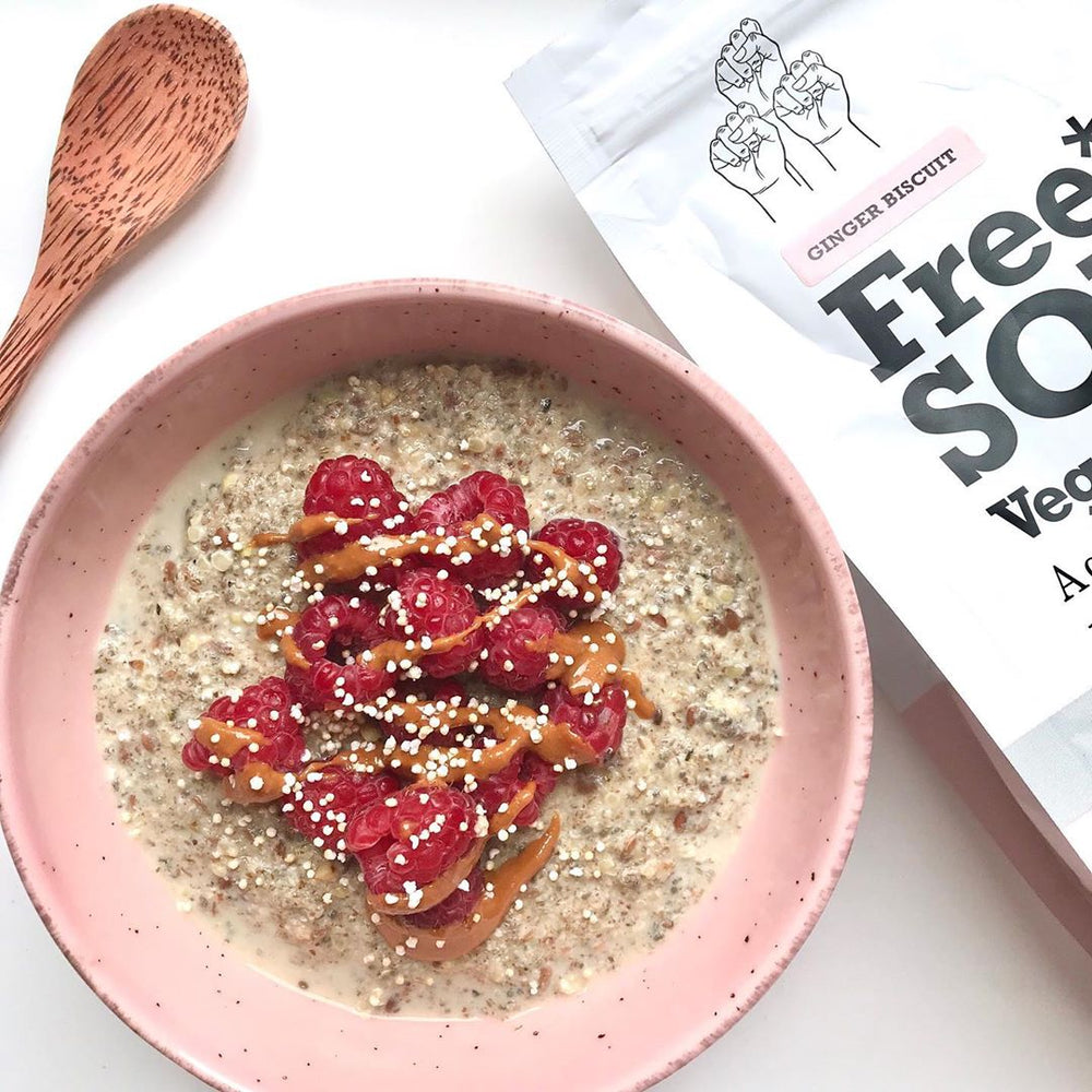 A pink bowl of oats with raspberries and a golden spread next to a wooden spoon