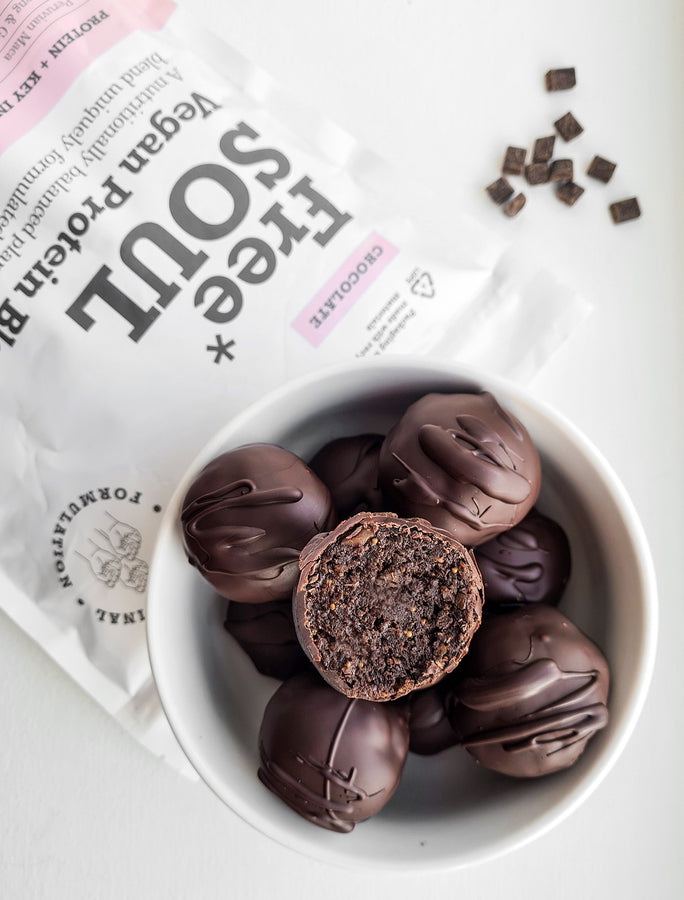 Chocolate protein balls in a white bowl covered in a thick layer of chocolate