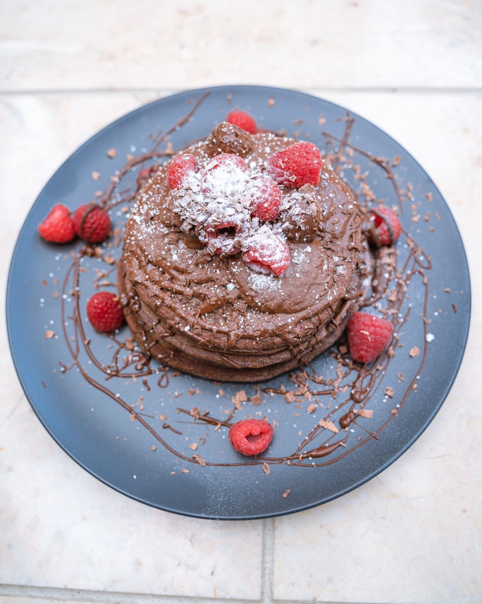 Chocolate pancakes stacked on a blue plate with fresh raspberries