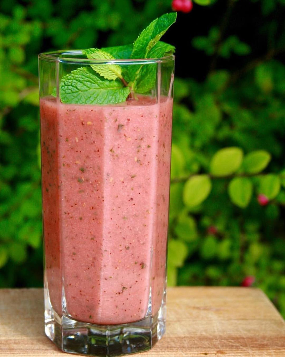 A pink smoothie, topped with a fresh mint spring before a green bushel