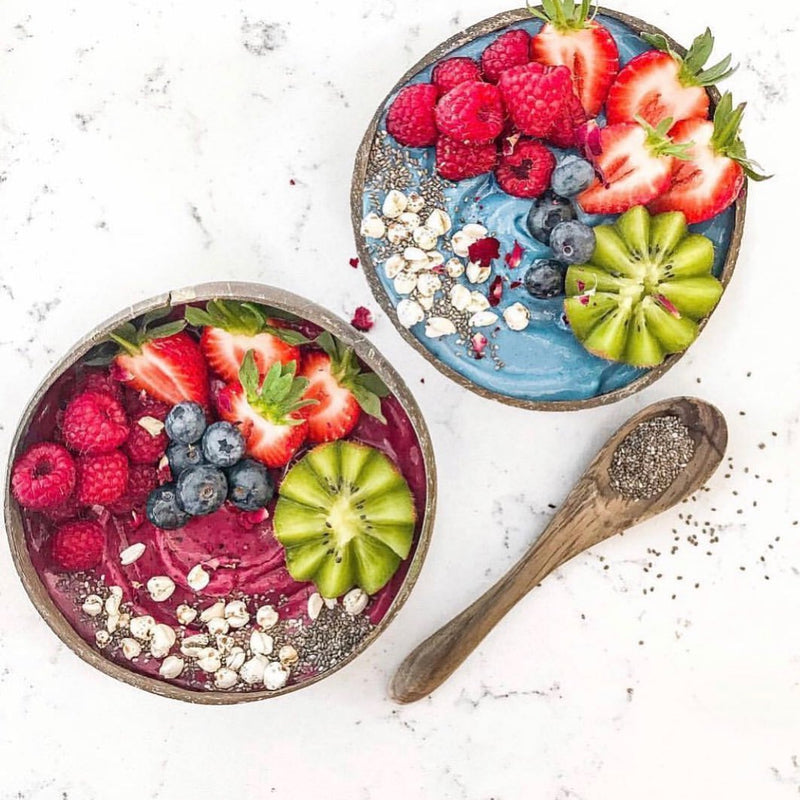 Two coconut bowls with purple and blue smoothies in each one