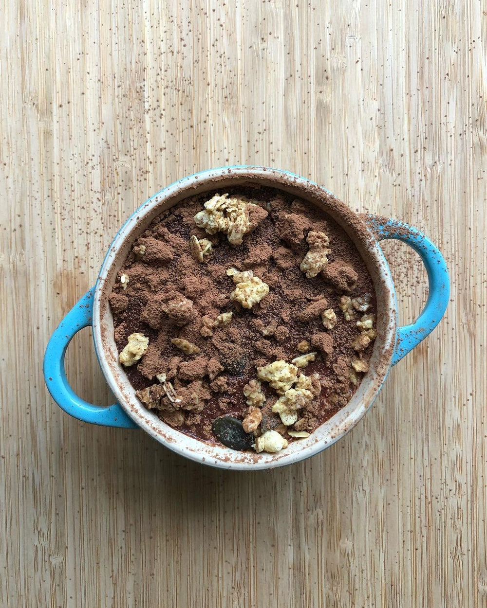 Blue baking dish filled with chocolate dessert topped with walnuts and coco powder