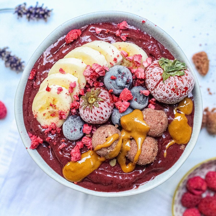 White bowl filled with purple smoothie, protein balls, frozen fruit and bananas