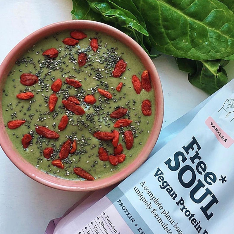 Green smoothie bowl next to fresh spinach and a bag of protein powder