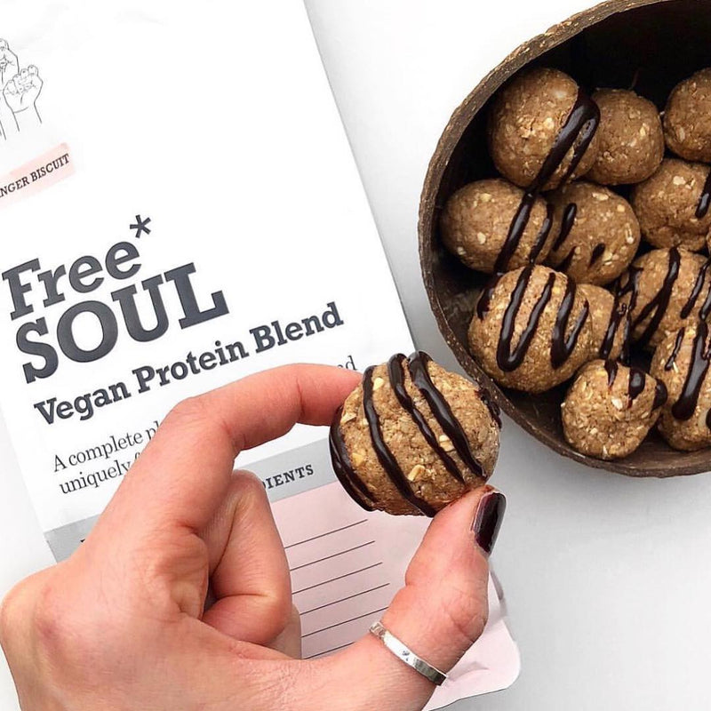 Two fingers wth brown nail polish holding a protein ball with oats and a chocolate drizzle