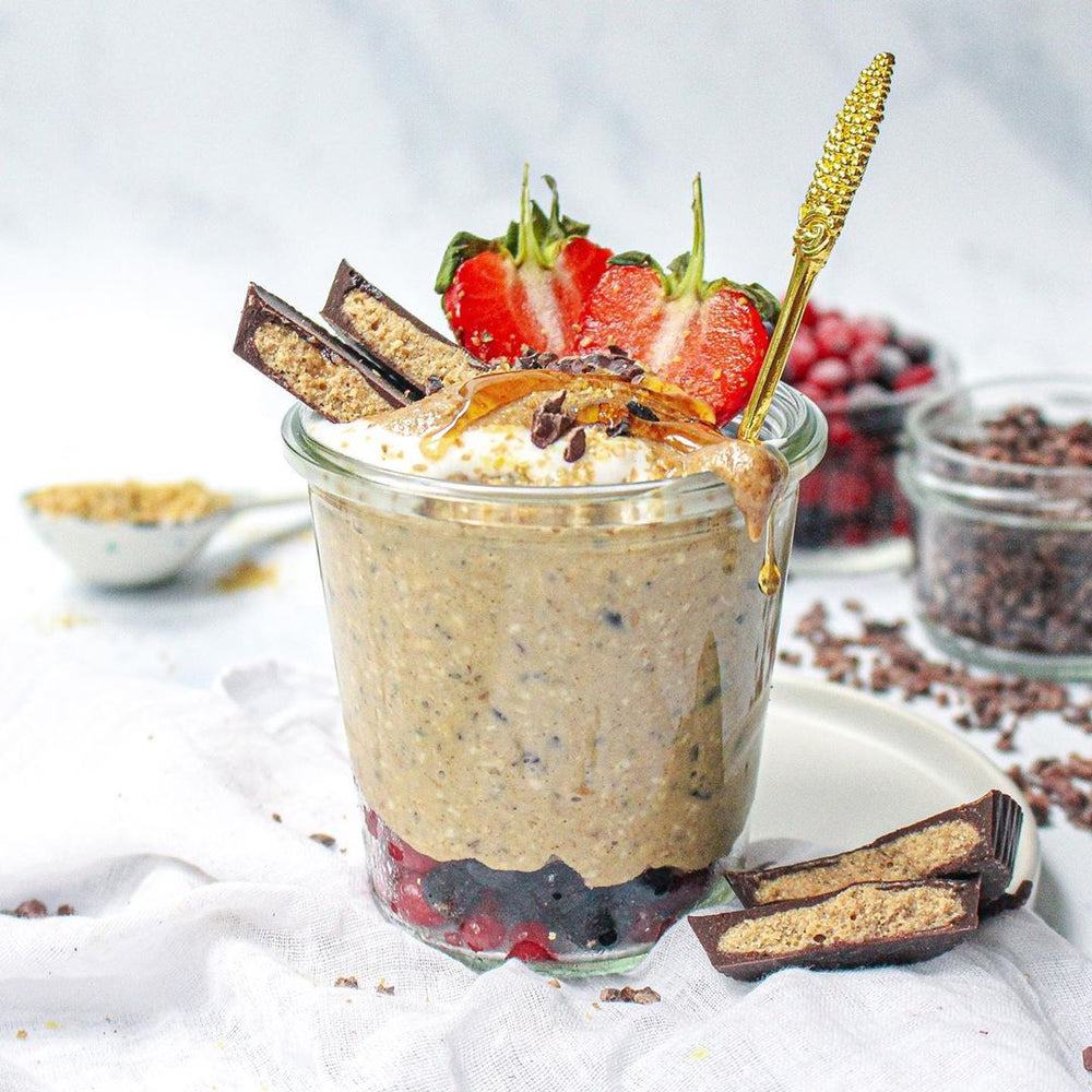 A glass filled with a protein smoothie and topped with fruits, chooclate and syrup