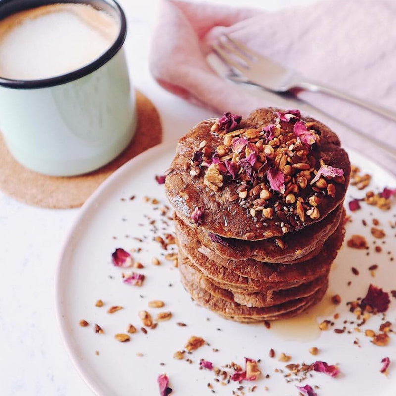 A stack of chocolate pancakes topepd with nuts next to a mug of coffee