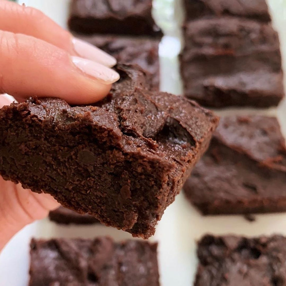 Close up of a hand with pink finger nails holding a gooey brownie