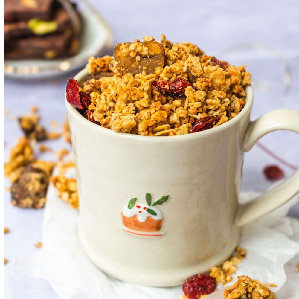 Cream coloured mug filled with golden granola, dried fuits and nuts