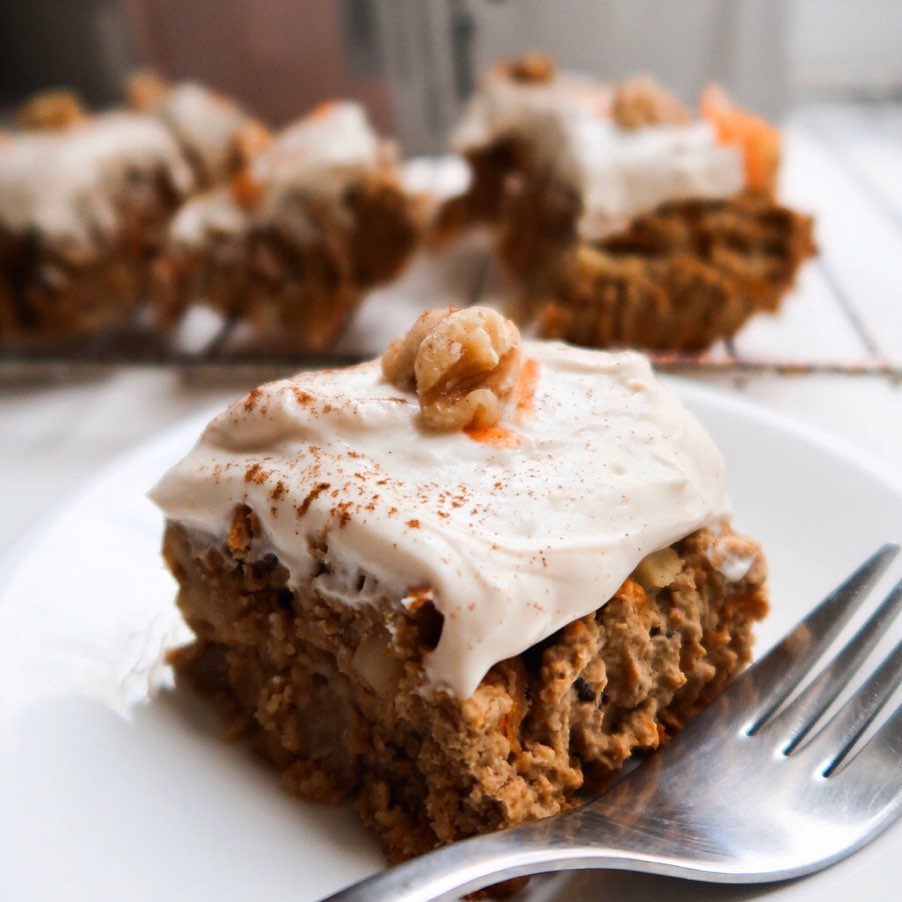 A slice of carrot cake on a white plate next to a silver fork