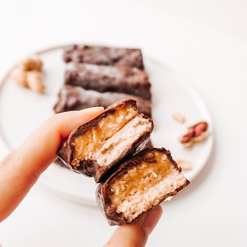 Two fingers holding a plant-based protein bar coated in chocolate