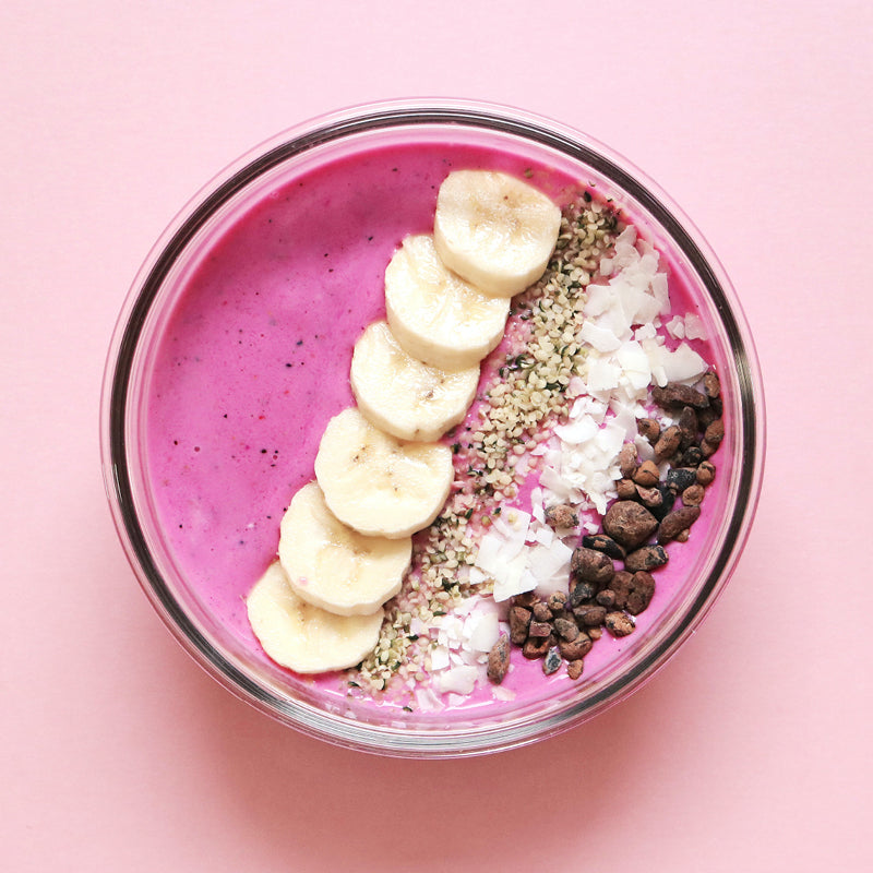 A glass bowl filled with pink smoothies, cut bananas and coconut shavings