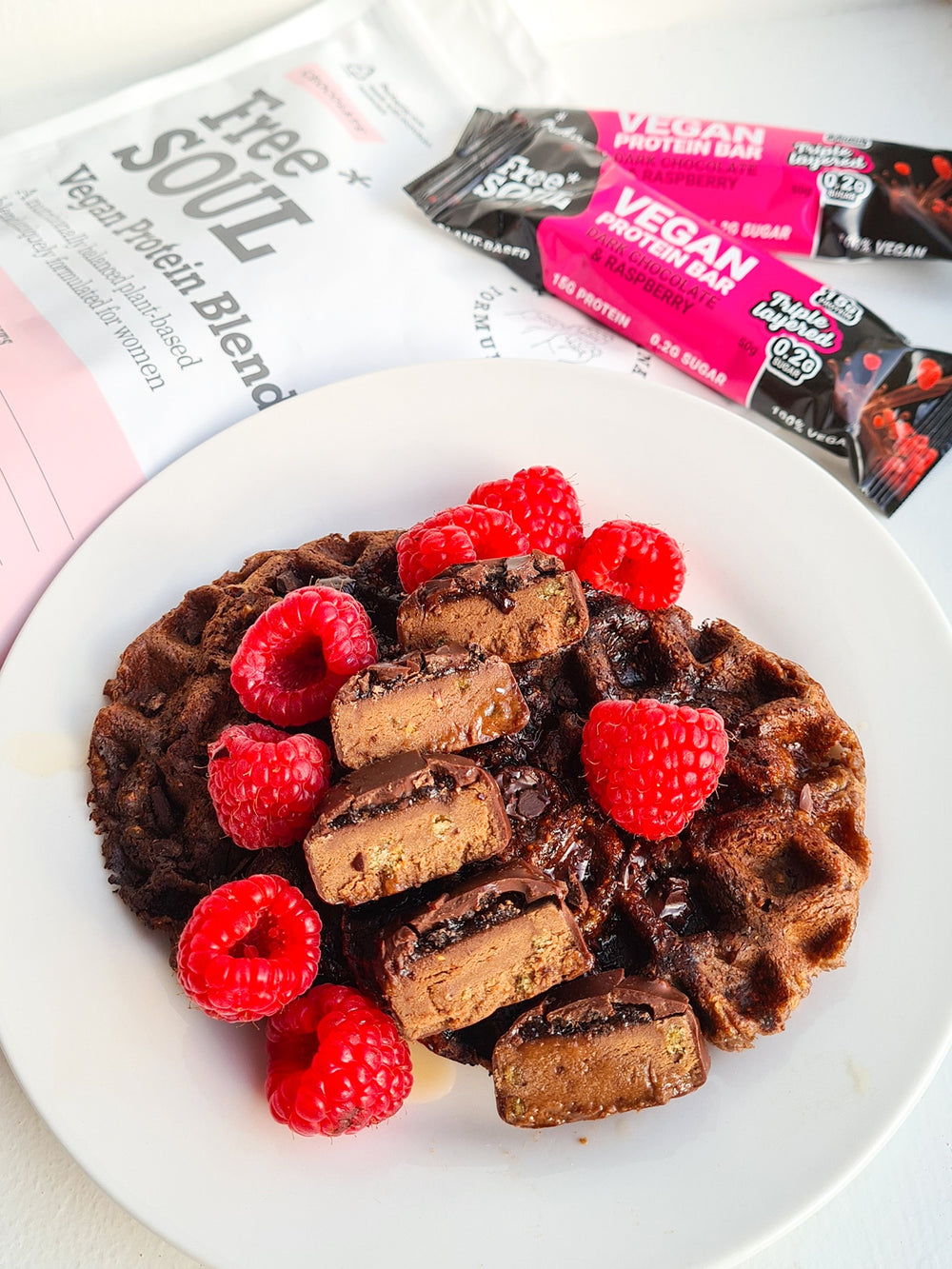 Chocolate pancakes topped with raspberries and a chopped protein bar