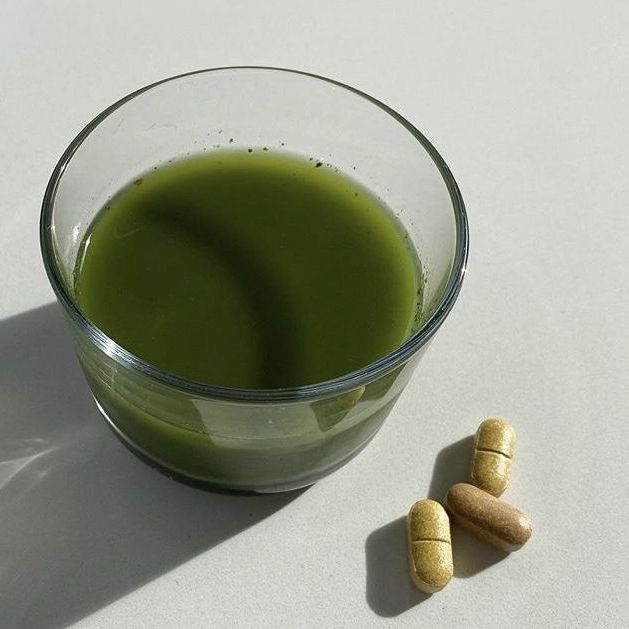 Cup filled with Greens juice next to 3 supplement capsules