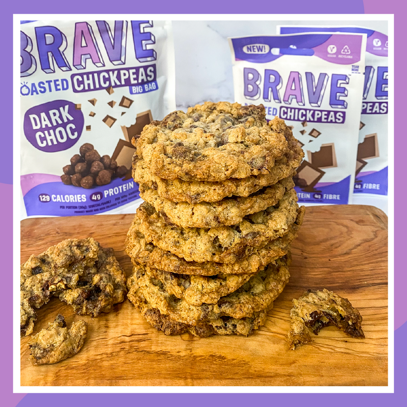 Stack of dark chocolate chip cookies on wooden table with Brave roasted chickpeas packaging in the background