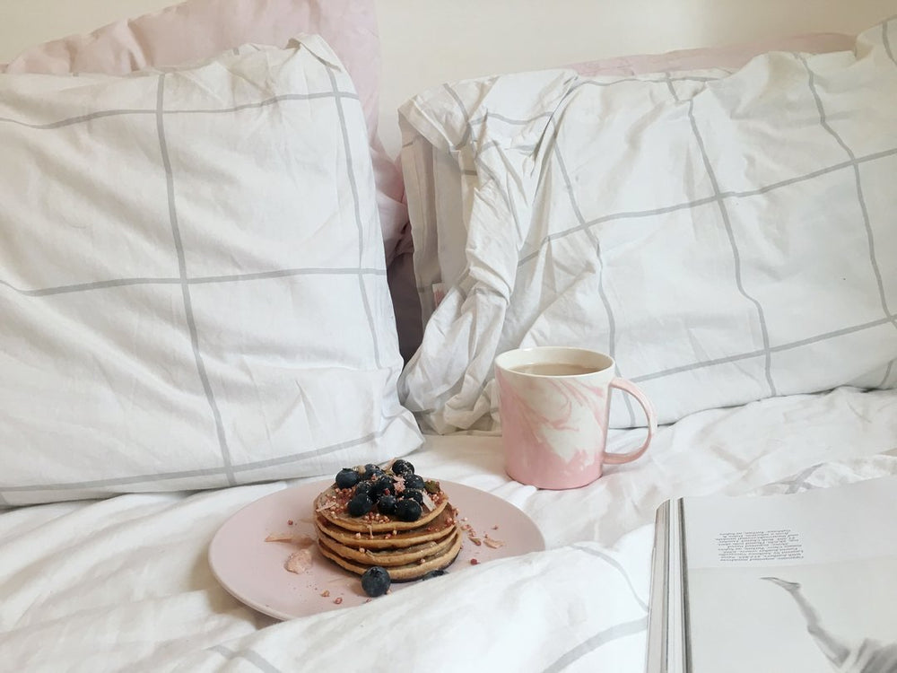 A stack of blueberry pancakes on a white duvet and pillowcase set