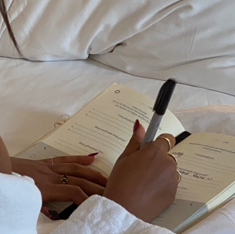 Person writing in gratitude journal with a sharpie on white bed sheets