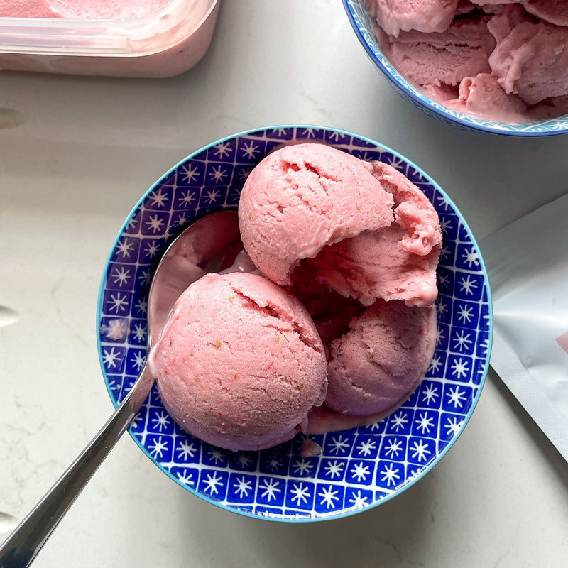 Three scoops of strawberry ice cream in a blue bowl with a spoon