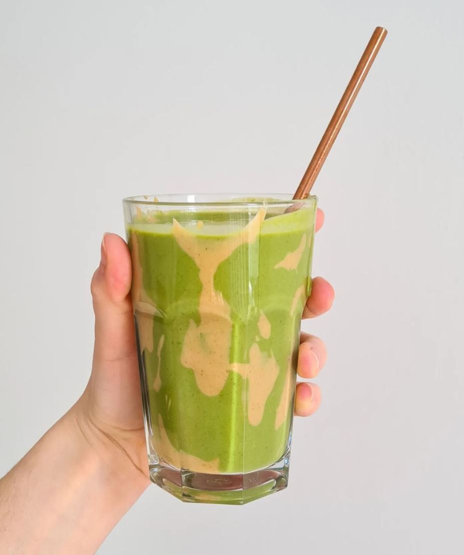 A hand holding a glass of vanilla and green smoothie