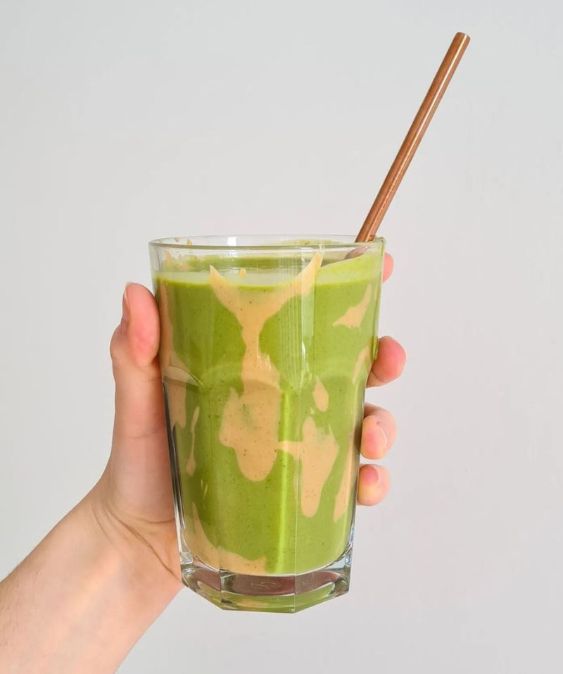 A hand holding a glass of vanilla and green smoothie