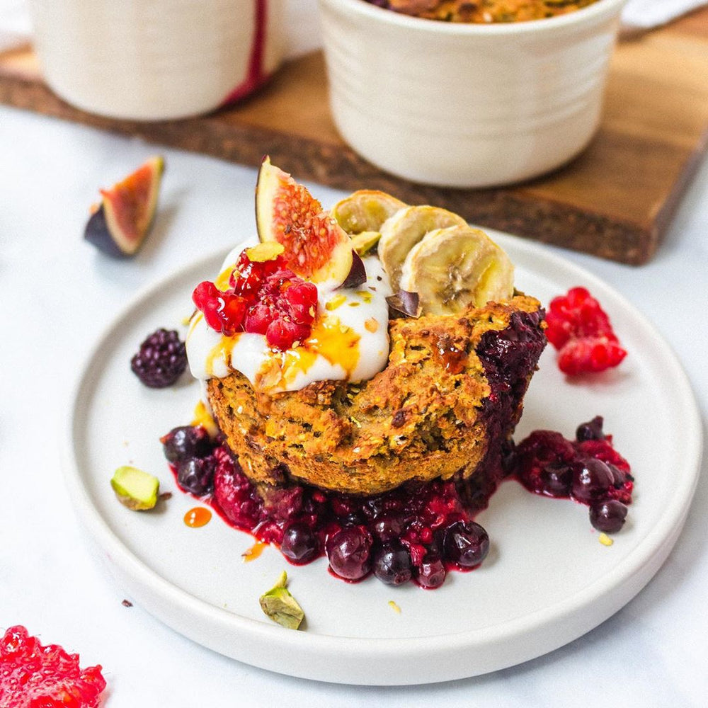 A white plate topped with a baked good, purple berries and chopped fruit