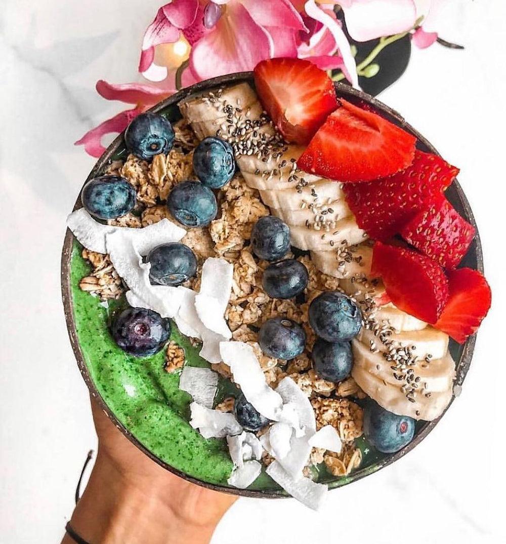 Coconut bowl filled with green smoothie, chopped fruit and seeds