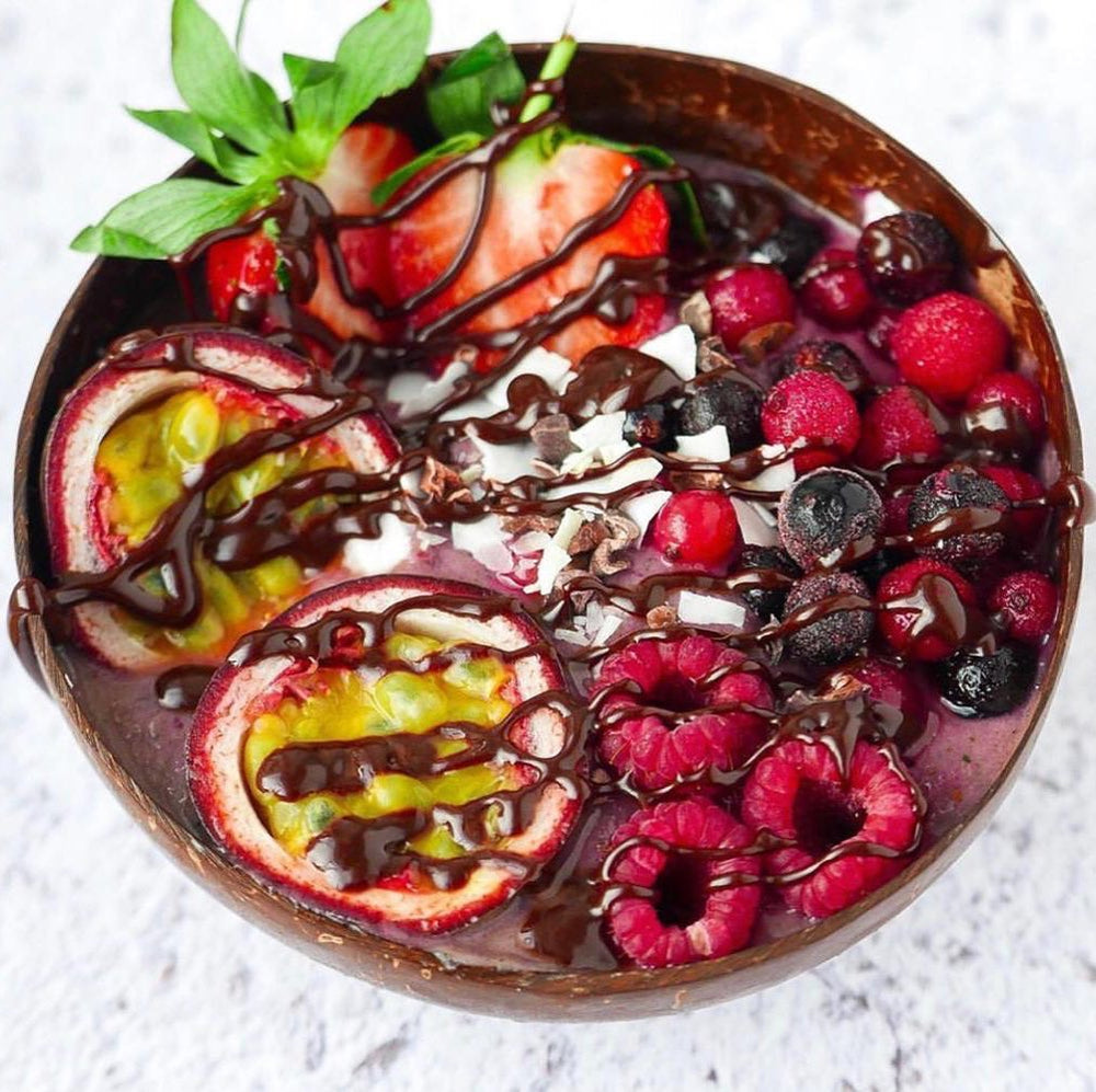 Coconut bowl filled with thick smoothie, fresh berries, a passionfuit and chocolate drizze