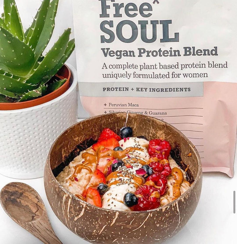 Coconut bowl and spoon filled with oats in front of Free Soul protein powder