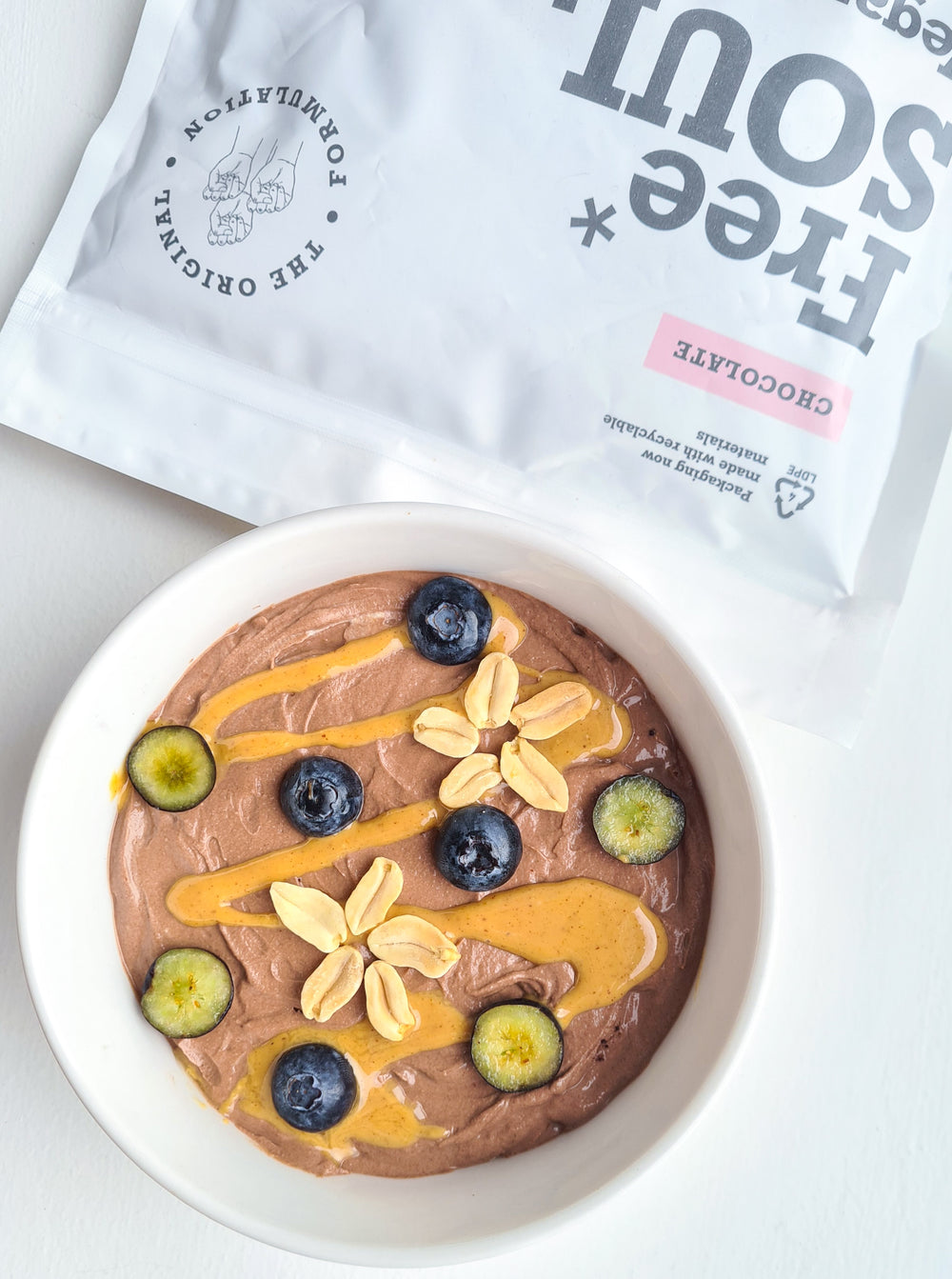 A bowl of chocolate protein mousse topped with peanut butter, peanuts and blueberries