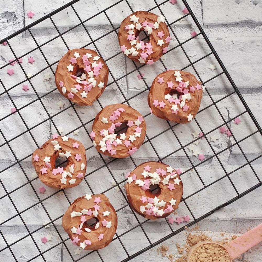 Miniture doughnuts with pink and white star sprinkles on a black cooling rack
