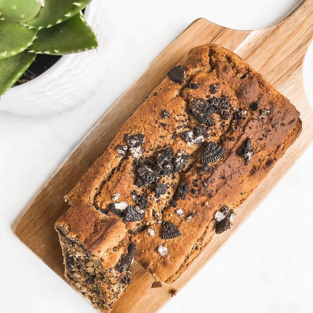 A wooden cutting board with a loaf of oreo-covered banana bread on top
