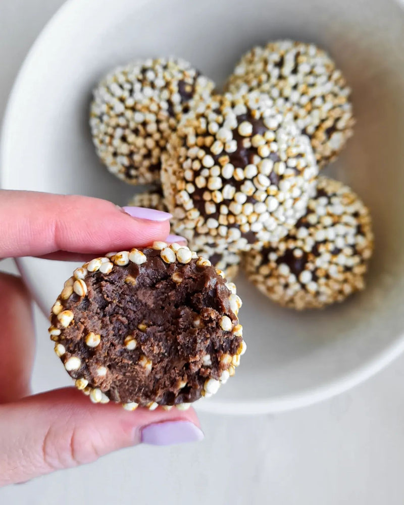 A hand holding chocolate protein balls rolled in crispy puffs