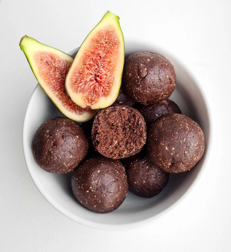 Chocolate protein balls with one half eaten in a bowl next to a fig