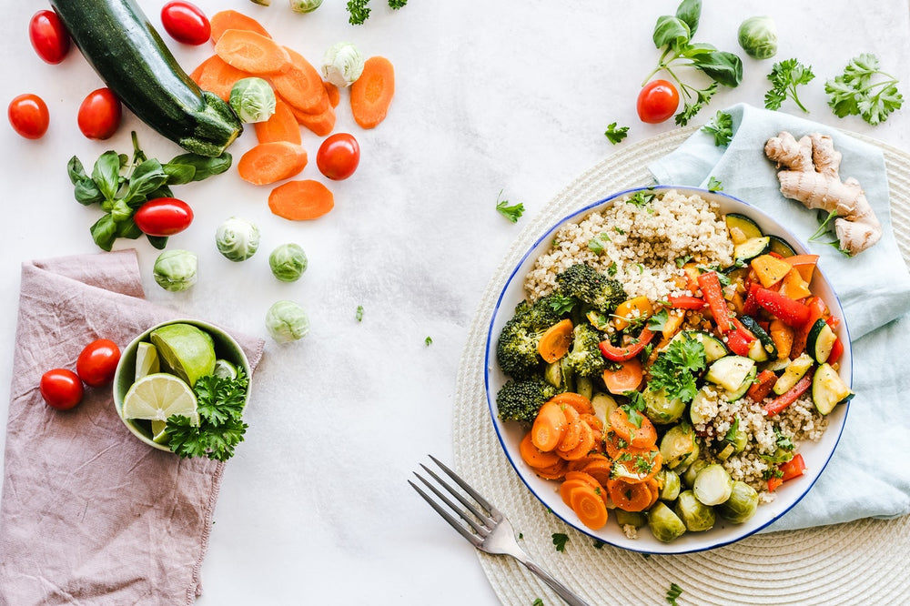 A bowl of chopped vegetables and cousous next to limes, corriander and a zucchini