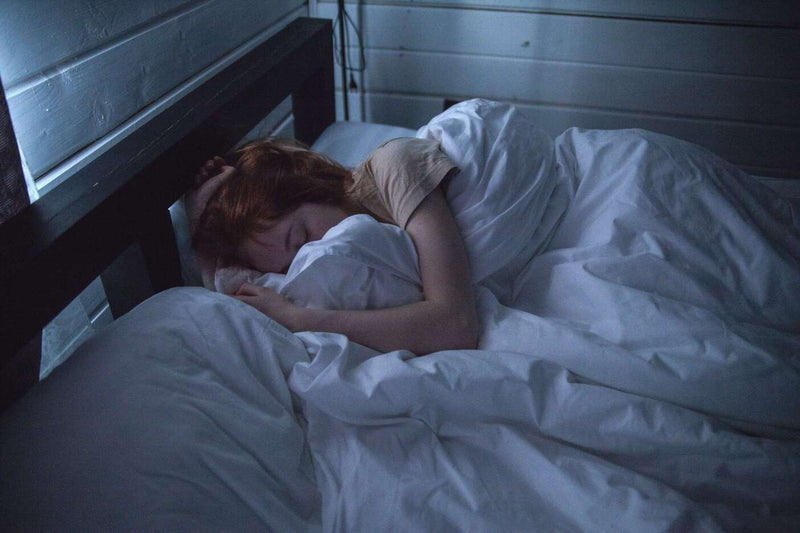 Person sleeping in a white bed in a dark room