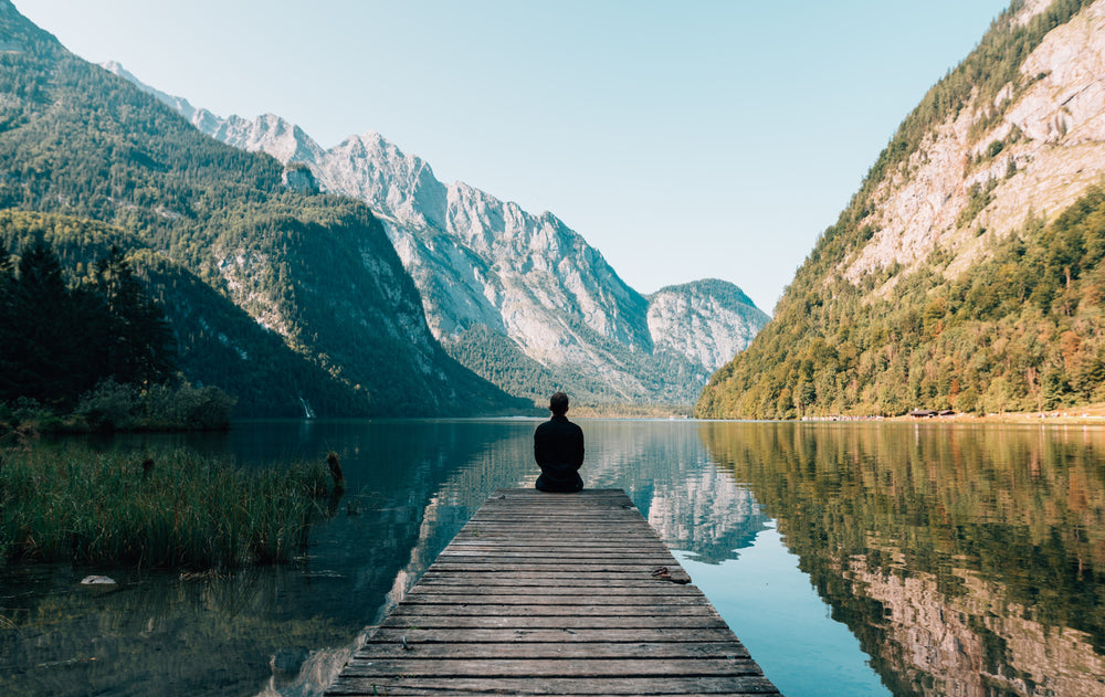 The silhouette of a person sitting on a ledge overlooking trees and mountains 