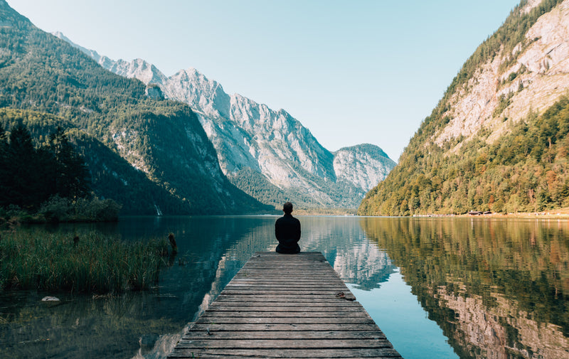 The silhouette of a person sitting on a ledge overlooking trees and mountains 